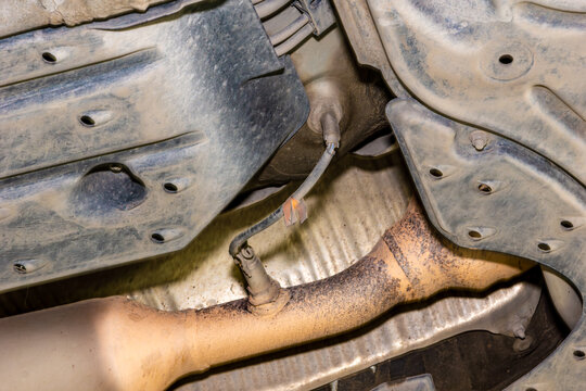 Black plastic undertray and oxygen sensor mounted on sooty exhaust pipe visible during diagnostic maintenance. selective focus