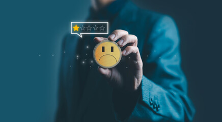 A businessman holding a wooden sad face icon with a low one-star rating, symbolizing customer dissatisfaction, negative feedback, poor service experience, and declining quality in modern business.