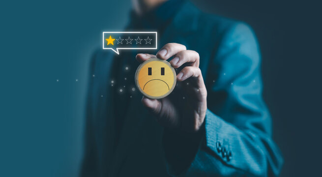 A businessman holding a wooden sad face icon with a low one-star rating, symbolizing customer dissatisfaction, negative feedback, poor service experience, and declining quality in modern business.
