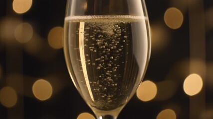 A close-up of a champagne flute filled with sparkling wine, with bubbles rising against a dark background with golden bokeh lights. - Powered by Adobe