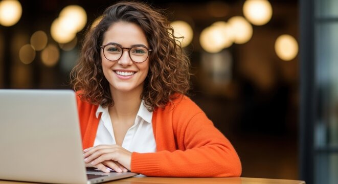 Happy young woman wearing stylish glasses smiling while working on laptop at cafe - Powered by Adobe