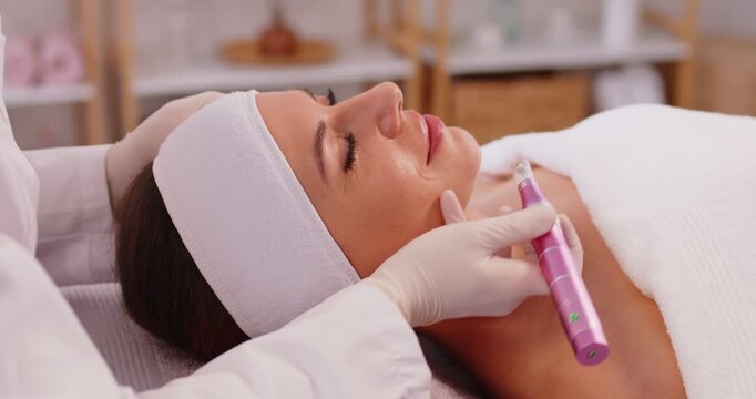 Beautiful woman receiving apparatus facial treatment procedure from cosmetologist in beauty wellness spa salon. Beautician consulting client in cosmetology cabinet. Skin care concept. 4k video.