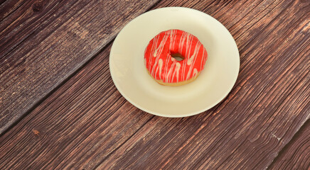 A fresh donut with red berry glaze in a round ceramic plate on a wooden table.