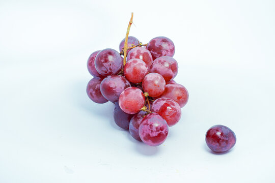 Lush bunch of fresh deep red and purple grapes with a single fallen berry on a clean white background, ideal for wine and health themes - Powered by Adobe