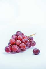 Lush bunch of fresh deep red and purple grapes with a single fallen berry on a clean white background, ideal for wine and health themes