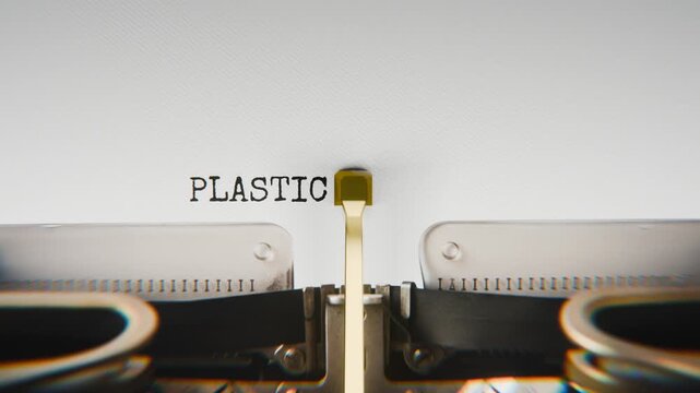 Old mechanical typewriter typing Plastic Reuse in a close-up view, with metal letters striking the white paper.