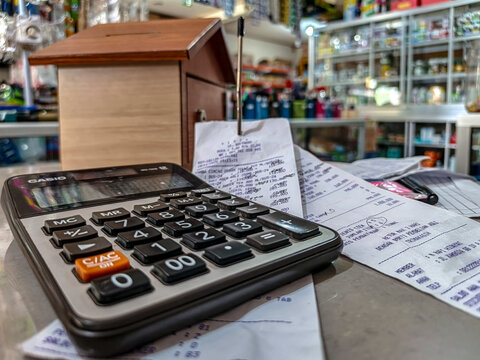 A close-up image of a calculator placed on a counter surrounded by printed receipts and financial notes inside a small retail shop