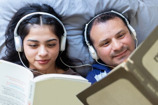 Father and daughter enjoy listening to music and reading books at home