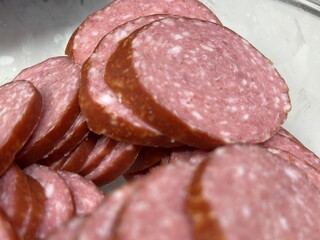 Sliced smoked sausage in a glass bowl, ready for cooking or serving. Close-up food photography on a light kitchen background.