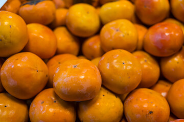 Freshly harvested ripe orange persimmons piled up at a market stall, showing their smooth skin and calyx.