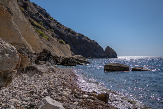 Beach Cliffs Sea rocky shoreline with sparkling blue sea and steep cliffs under a clear sky featuring a natural rock arch - Powered by Adobe