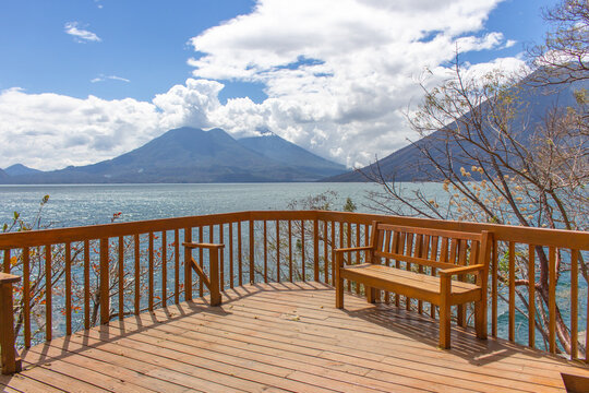 Lake Atitlan wooden deck with bench overlooking volcanic mountains sparkling blue water serene lakeside view peaceful nature landscape relaxing outdoor scene travel photography scenic panoramic beauty - Powered by Adobe
