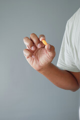 Hand holding a yellow pill against a gray background