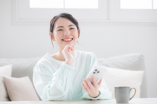 スマホ持つ女性が笑顔で幸せ感じる室内のかわいい日本人アジア人の明るい日常シーン カメラ目線