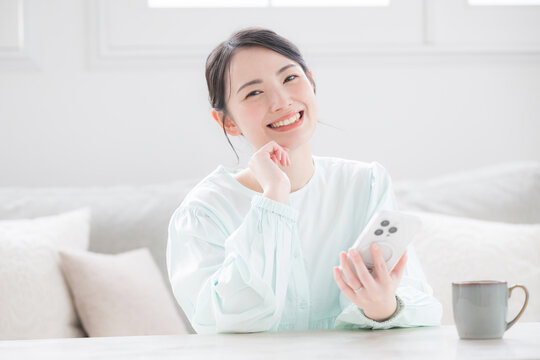 スマホ持つ女性が笑顔で幸せ感じる室内のかわいい日本人アジア人の明るい日常シーン カメラ目線