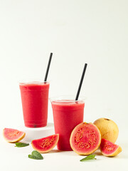 two plastic cups of fresh guava juice surrounded by guava slices on a white background
