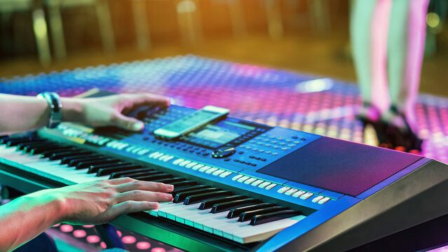 Hands of male musician press digital electronic keyboard synthesizers on concert stage. Pianist man hands play the keys of electronic piano. Piano music pianist hand playing. Selective focus on hand. - Powered by Adobe