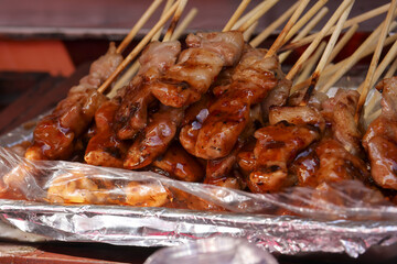 Delicious grilled pork skewers with savory sauce on foil. Close up of Asian street food barbecue, traditional and appetizing snack at market for tasty meal