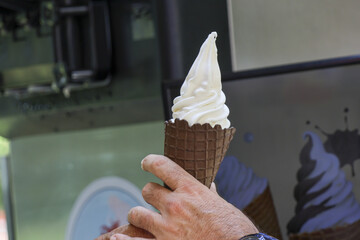 Person hand holds delicious soft serve vanilla ice cream in crispy waffle cone. refreshing summer...