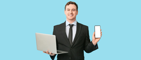 Happy young businessman with laptop and mobile phone on blue background