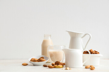 Glass and jugs of fresh almond milk with nuts on white background