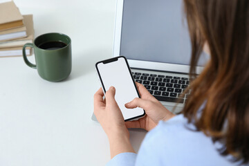 Young woman using blank mobile phone at table in office, closeup