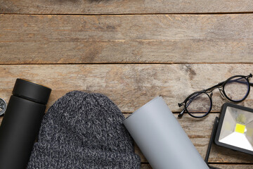 Warm hat, thermos, map, glasses and flashlight on wooden background