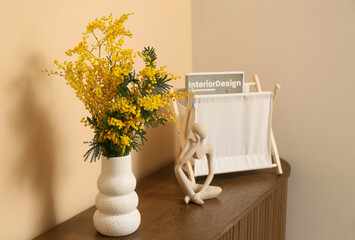 Vase with mimosa flowers, statuette and magazine stand on shelf in room