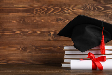 Mortar board with stack of books and diploma on wooden background