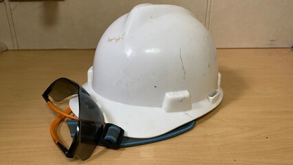  a pair of personal protective equipment (PPE), helmet and glasses, which are placed on the surface of a wooden table.