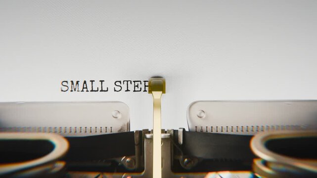 Old mechanical typewriter typing Small Steps Make Big Changes in a close-up view, with metal letters striking the white paper.