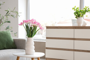 Vase with tulips on table in light living room