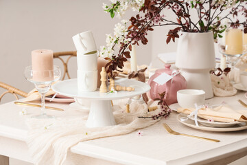 Table setting with blossoming branches, candles and chess pieces in room, closeup