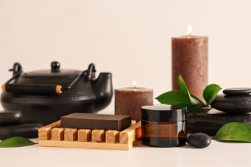 Spa composition with teapot, cosmetic products and burning candles on light table