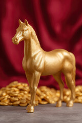 Golden horse figurine standing on gray surface with red velvet fabric background, symbolizing wealth and luxury, elegant and decorative, perfect for interior design or festive celebration