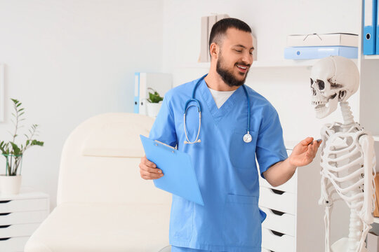 Male doctor with clipboard and human skeleton model in clinic