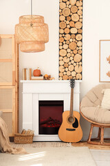 Naklejka premium Interior of living room with armchair, closet, guitar, fireplace and autumn home decor near white wall