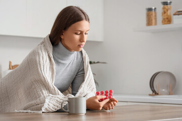 Ill young woman with throat lozenges and cup of tea at table in kitchen