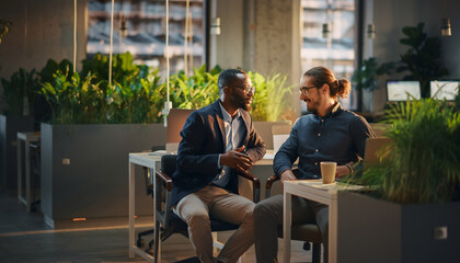 Business conversation between coworkers in relaxed and positive mood, modern office with greenery, natural light, casual attire, teamwork, friendly atmosphere, collaboration