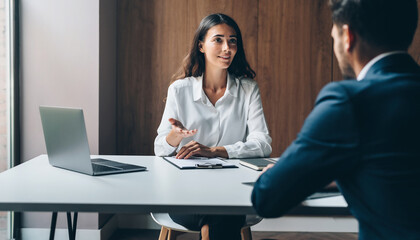 Businesswoman explaining project details to colleague in modern office, natural light, minimal clean workspace, professional atmosphere, teamwork, communication, confidence
