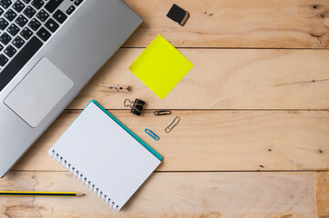 Laptop with notebook, paper clips, notepad and pencil on wooden table, top view shot