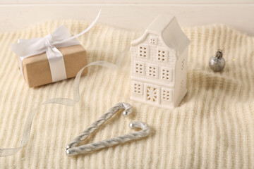 Decorative house with Christmas gift box, candy canes and sweater on white wooden background