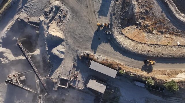 Bull dozer driving into a gravel crushing plant at first light. Dust rising from plant in first light. Directly overhead view.
