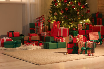 Many different gift boxes with decorations near Christmas tree in festive room at night