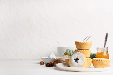 Plate with tasty Christmas mince pies, jar of honey and ceramic juicer on white background