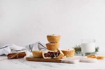 Board with tasty Christmas mince pies, glass of milk and cinnamon on grunge table against white background