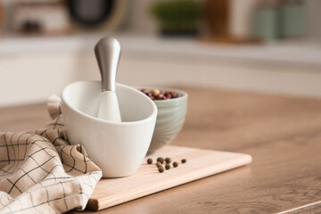 Mortar with pestle and peppercorns on table in kitchen, closeup