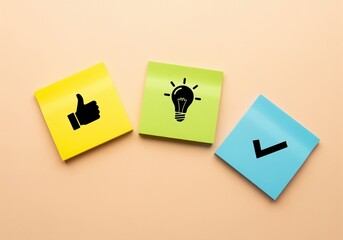 Thumbs up, light bulb, and checkmark icons on colorful sticky notes symbolizing idea and success.