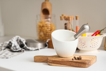 Mortar with pestle and peppercorns on counter in kitchen, closeup