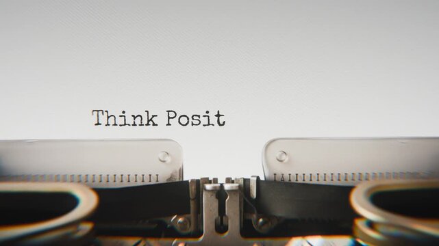 Old mechanical typewriter typing Think Positive in a close-up view, with metal letters striking the white paper.